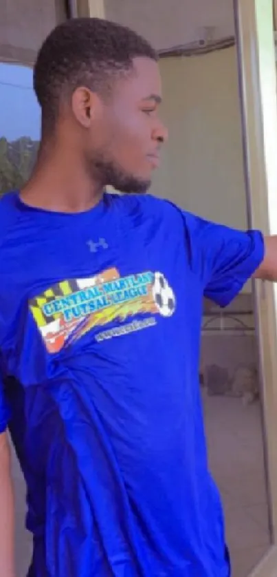 Young man in a bright blue sports shirt standing outside.