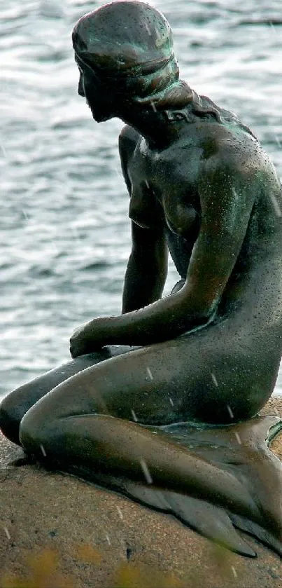 Mermaid statue sitting on rock by the sea, serene background.