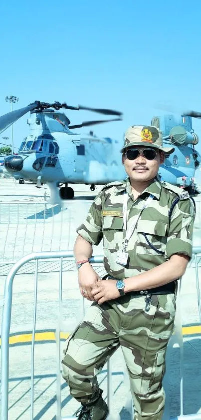 Soldier in camo with helicopter in background on clear day.