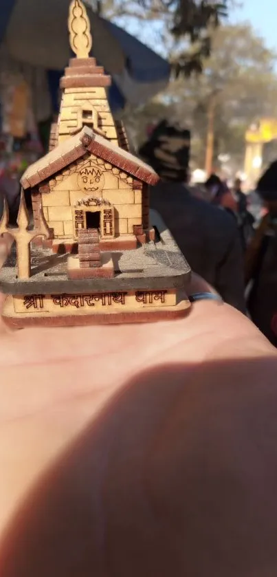 Miniature temple model held in a hand outdoors.