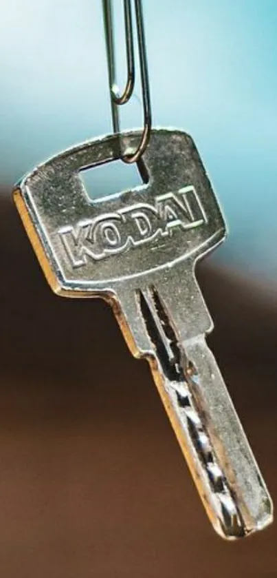 A close-up of a metallic silver key hanging with blurred blue background.