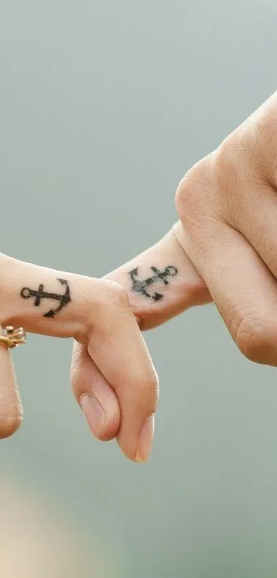 Two fingers with anchor tattoos on a beige background.