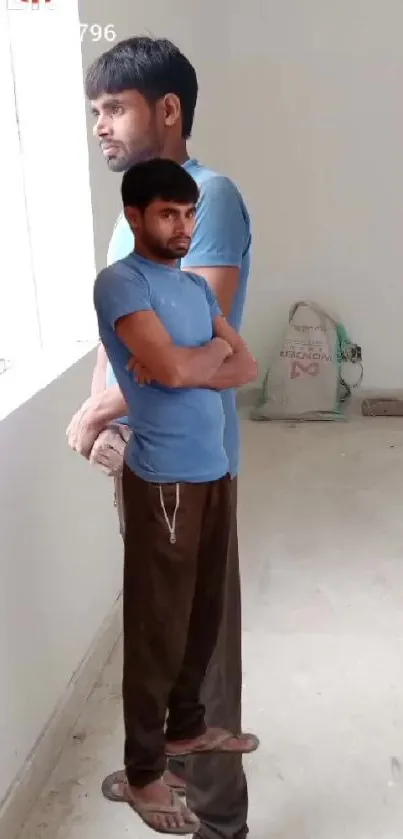 Man in blue shirt standing by a window indoors.