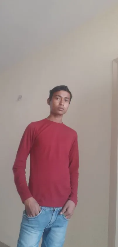 Casual young man in red shirt and jeans against a beige wall.