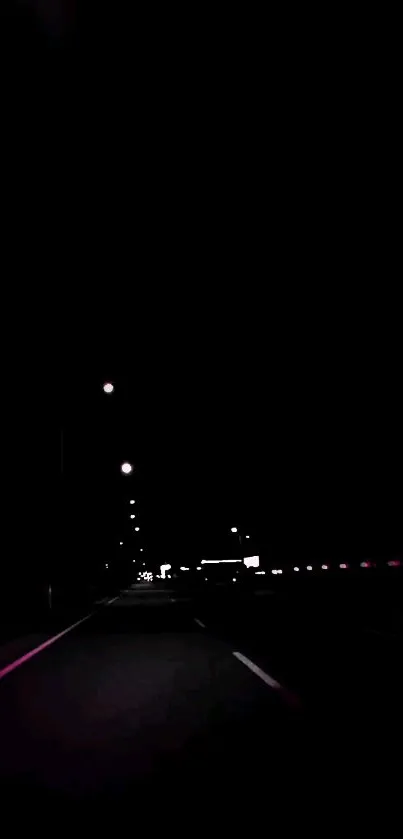 Dark highway illuminated by distant streetlights at night.