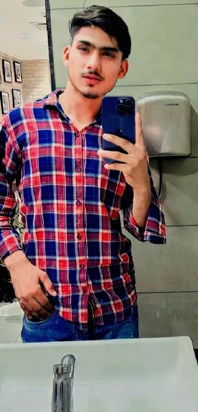 Person taking a mirror selfie in a red and blue plaid shirt.