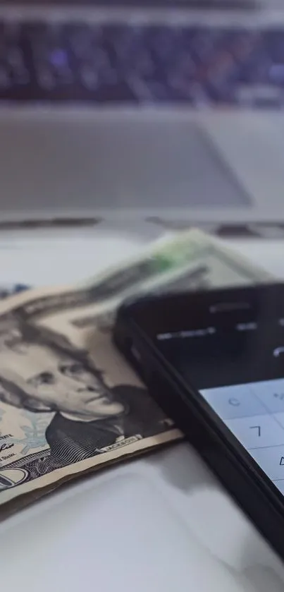 Smartphone with cash and laptop on desk.