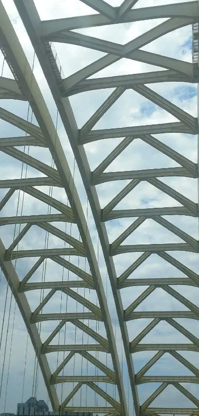 Modern architectural bridge with city skyline under a cloudy sky.