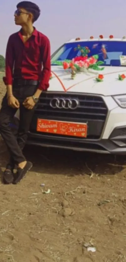 Young man in red shirt leans on decorated white car.