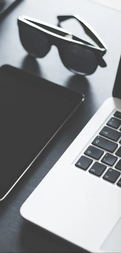 Modern workspace with laptop, tablet, and camera in grayscale setting.