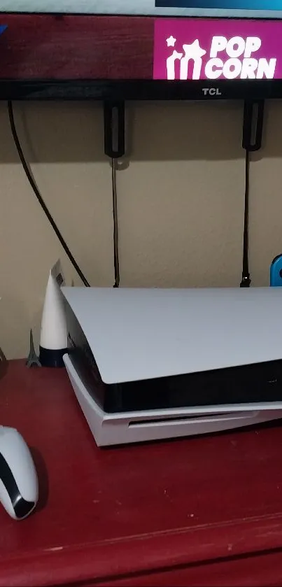 Modern gaming console and controllers on a red desk under a mounted TV.