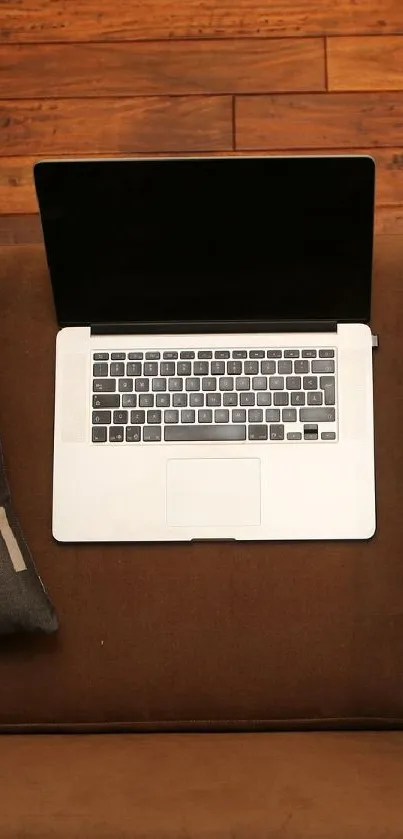 Laptop on a brown couch with wooden floor, minimalist style.