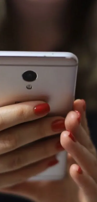 Hand holding a modern smartphone with red nails.