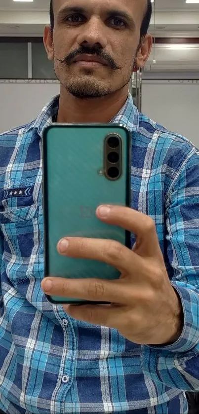 Man takes selfie with turquoise phone in barbershop mirror.