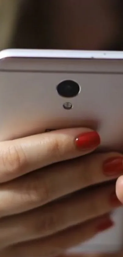 Hand holding a sleek smartphone with red nails.