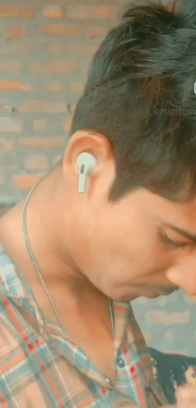 Young man with earbuds against brick backdrop.