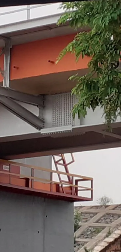 Modern urban bridge with orange and grey accents surrounded by greenery.