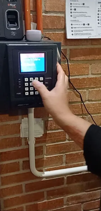 Hand interacting with a modern wall-mounted time clock on a brick wall.