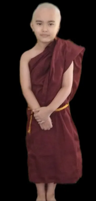 Young monk in maroon robe with a black background.