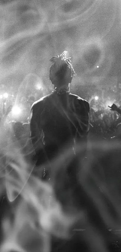 Silhouetted performer on stage in monochrome with cheering crowd.