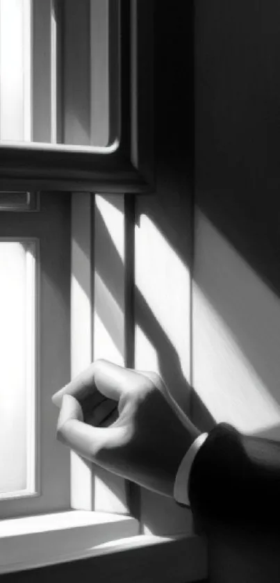 Monochrome hand reaching toward window with shadows and light play.