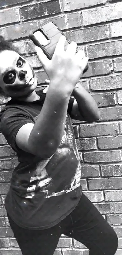 Black-and-white photo of a person taking a selfie with face paint and brick wall.