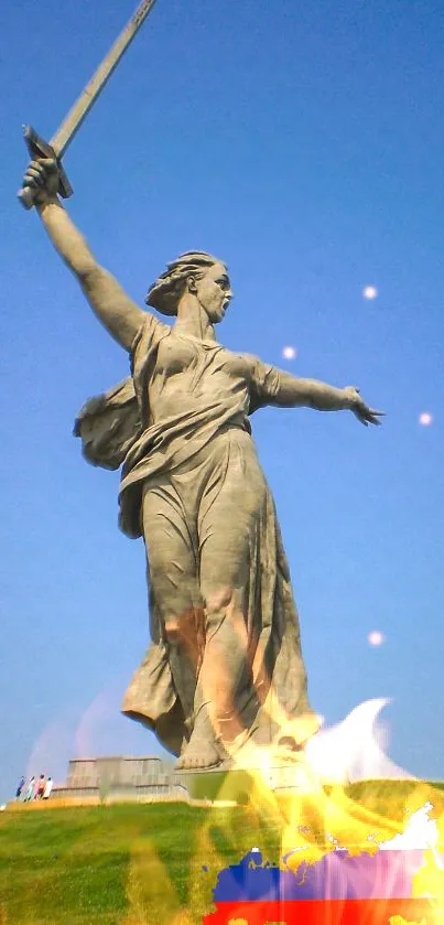 Statue with sword under clear blue sky in a vibrant landscape.