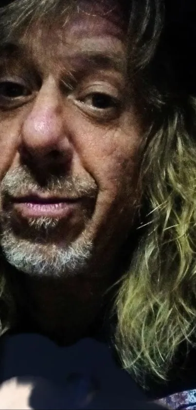 Portrait of man with long blonde hair in dark lighting; contemplative mood.