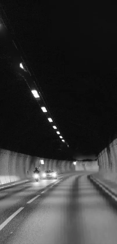 Moody tunnel road with faint car lights in dim black and white setting.