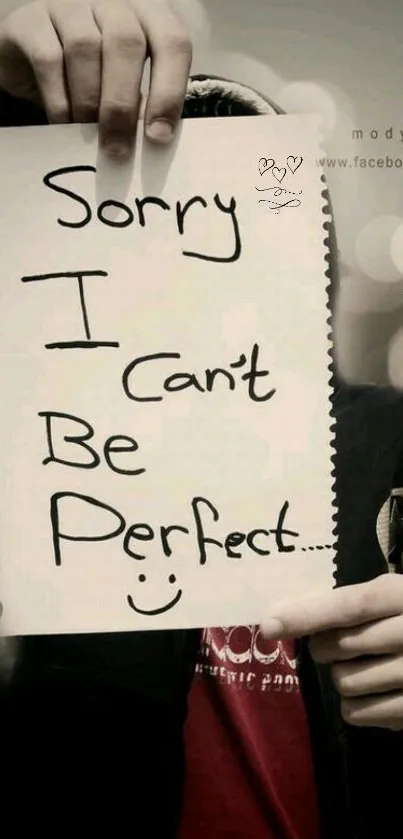 Hand holding a handwritten note saying 'Sorry I can't be perfect.'