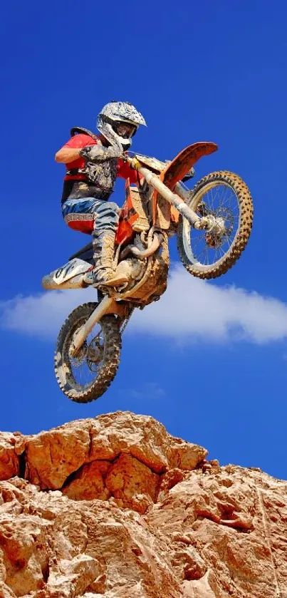 Motocross biker jumps against a vivid blue sky and rocky cliff.