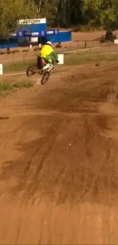 Motocross rider performing jump on a dirt track under a clear sky.