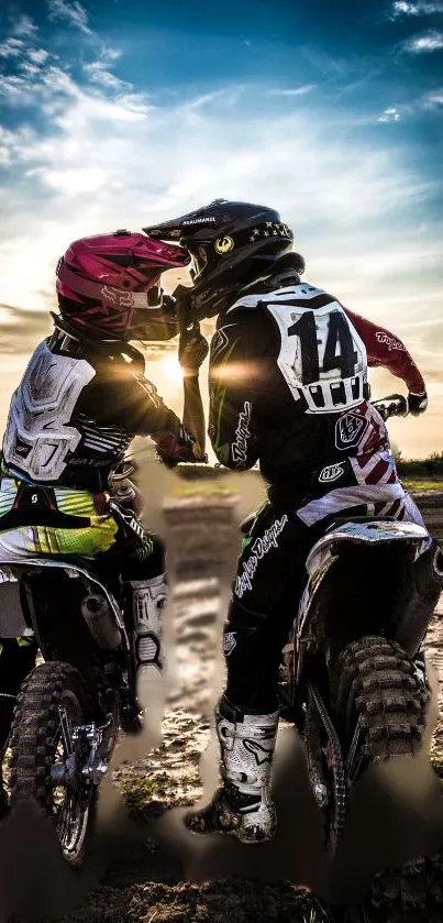 Two motocross riders sharing a moment under a sunset sky on a dirt track.