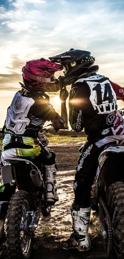 Two motocross riders share a moment at sunset, capturing adventure and camaraderie.