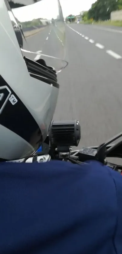 Motorbike rider on open road with helmet and scenic highway view.