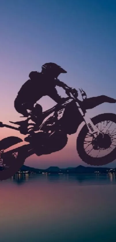 Motorbike silhouetted against sunset over water, vibrant blue sky.