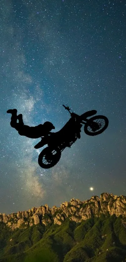 Motorbike stunt silhouette against starlit sky over mountains.