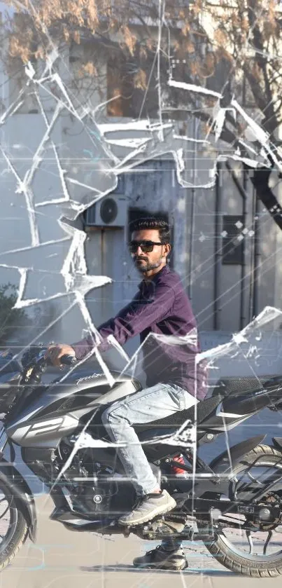 Man on motorcycle seen through shattered glass with urban background.