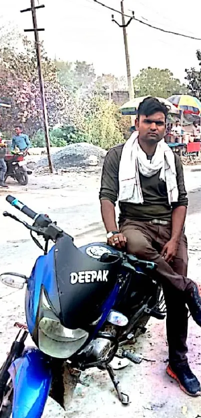 A man sits on a blue motorcycle in a vibrant street setting with people and bikes.