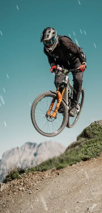 Mountain biker jumps on rocky trail against a scenic teal sky.