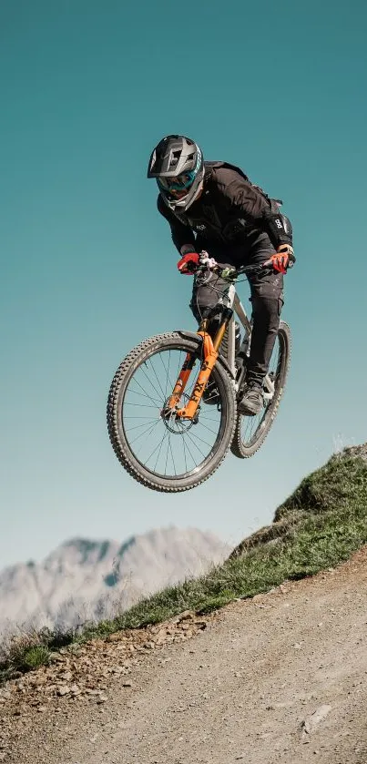 Cyclist mid-air on mountain track with clear sky backdrop.