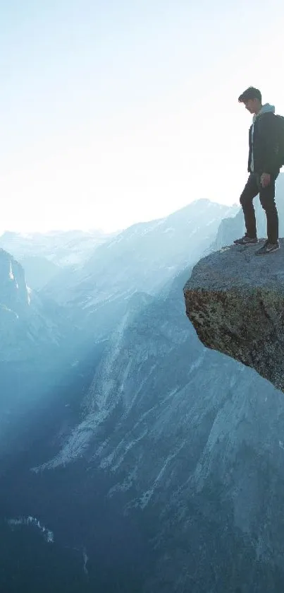 Lone hiker standing on mountain cliff with scenic view.