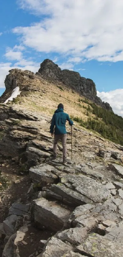 Person hiking on a rocky mountain with a clear blue sky and distant peaks.