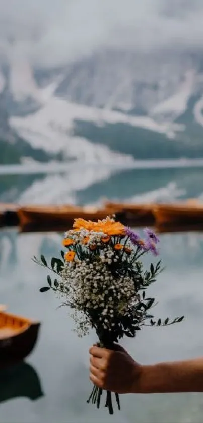 Hand holding a vibrant bouquet by a mountain lake.