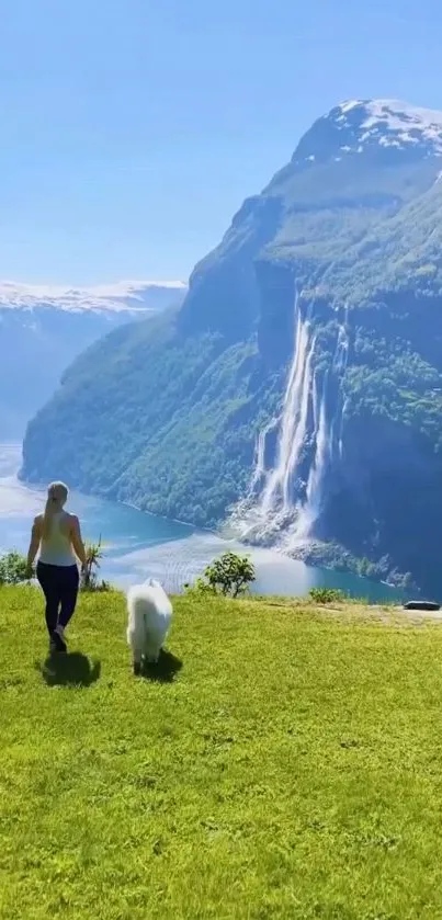 Woman and dog on a grassy hill overlooking a waterfall and mountain.