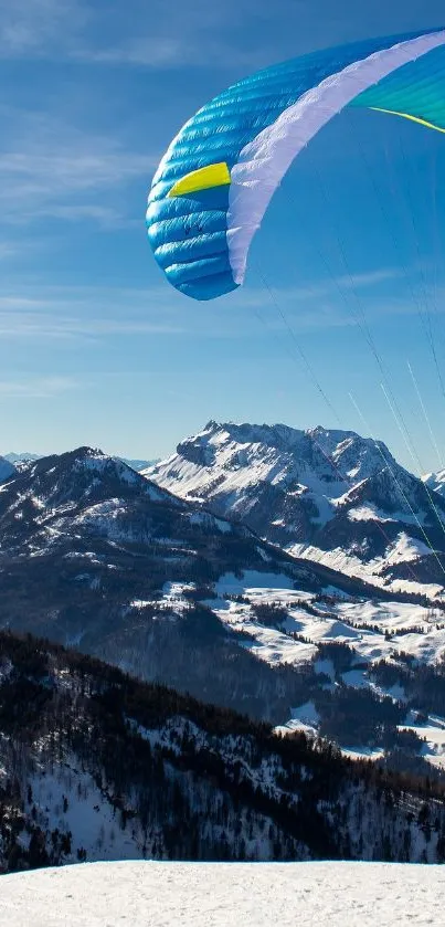 Paraglider over snow-capped mountains with clear blue skies.