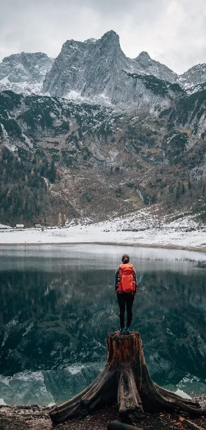 Hiker with red backpack gazing at serene mountain lake reflection.