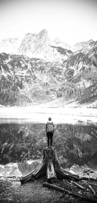 A lone figure stands before a reflective mountain lake under a vast, cloudy sky.