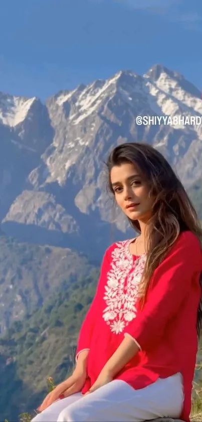 Woman in red sits in front of snowy mountains under a blue sky.