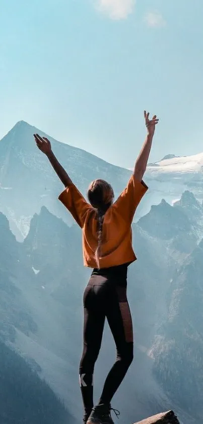 Person celebrating on a mountain with blue sky backdrop.